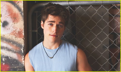 Froy Gutierrez wears a blue muscle shirt as he poses in front of a fence