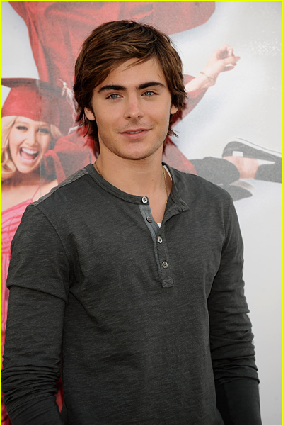 Zac Efron dresses casually while posing in front of a High School Musical 3 poster
