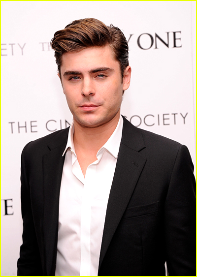 Zac Efron looks sauve in a black blazer and white shirt in front of a white backdrop