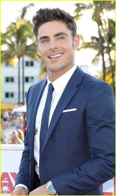 Zac Efron smiles in a suit at an outdoor event