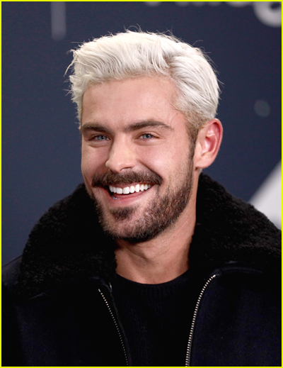 Zac Efron has a full beard and smiles, with white hair