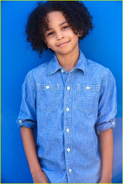 Christian Cote poses in front of a blue background in a denim shirt